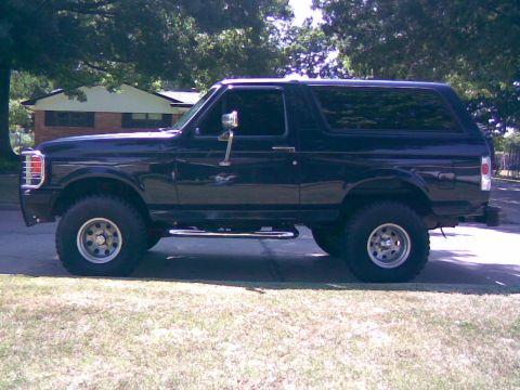 1991 Ford Bronco - A black Ford Bronco SUV is parked on a residential street, viewed from the side.