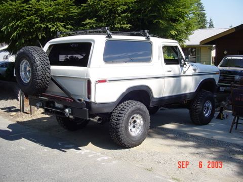 1989 Ford Bronco - This lifted white Ford Bronco is parked outside a house with a dark SUV behind it.