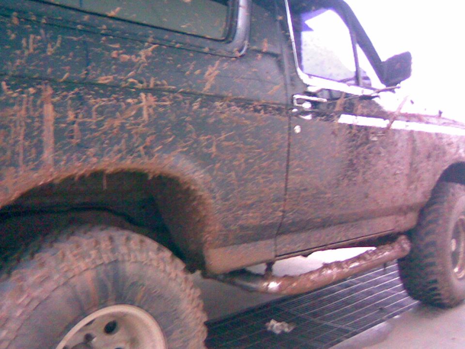 Mud-covered dark green 1992 Ford Bronco side view, showing fender flare, door, and running board