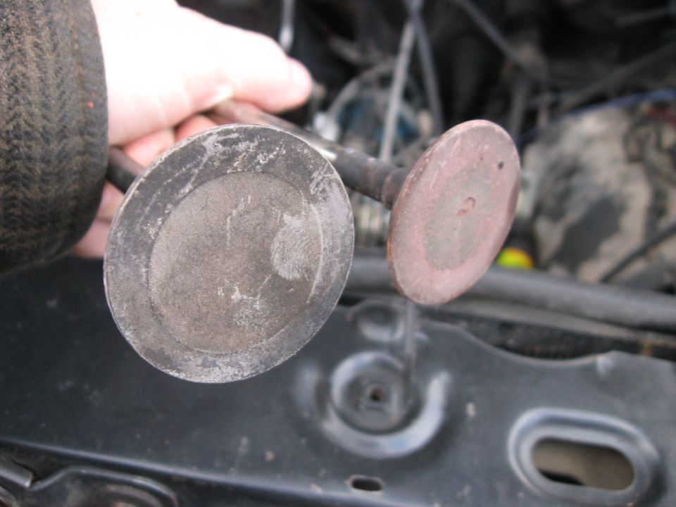 hand holding two engine valves, one with carbon buildup