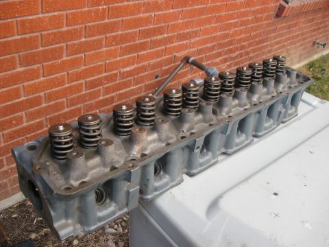 1981 Ford Bronco - A gray engine cylinder head with multiple valve springs is shown resting on a white surface against a brick wall.