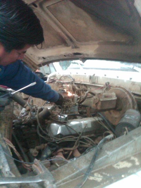 1982 Ford Bronco - Mechanic works on the carburetor in the engine bay of a 1982 Ford Bronco.