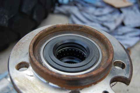 1994 Ford Bronco - Close-up of a removed steering-knuckle or axle spindle housing laid on concrete, showing surface rust on the machined bore, a needle-roller…