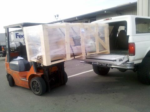 1995 Ford Bronco - A forklift is used to load large wooden crates into the cargo area of a white SUV.