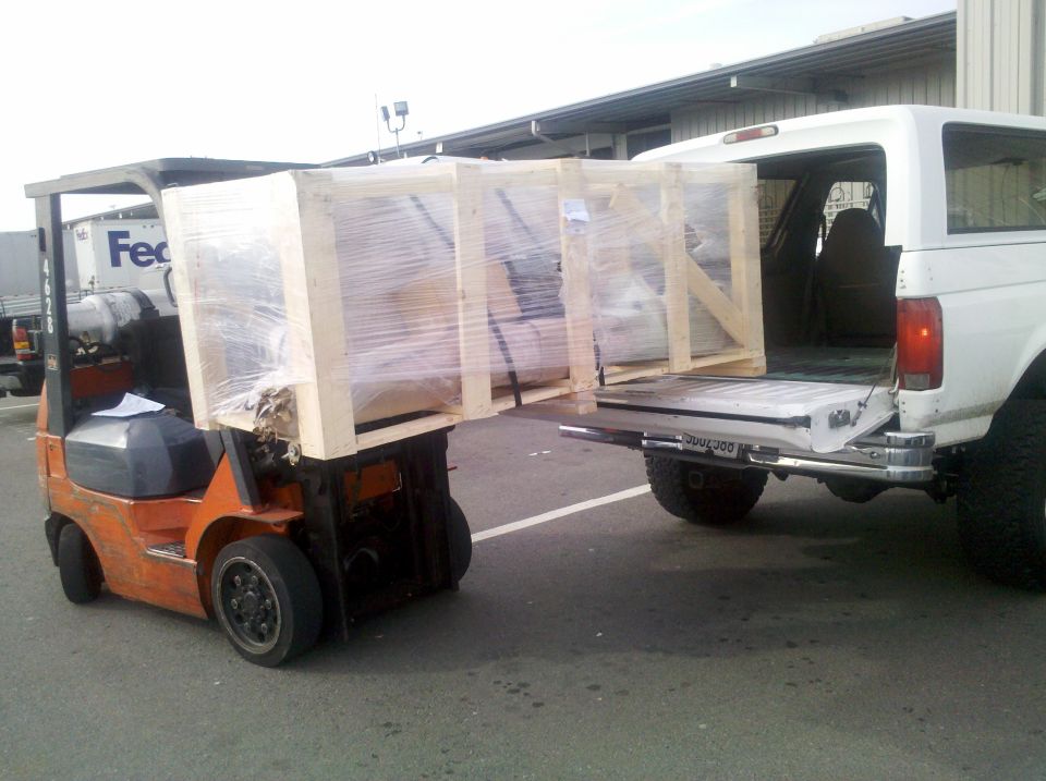 Forklift loading wooden crates into the back of a white SUV. The SUV has a spare tire mounted on the back