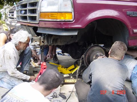 1989 Ford Bronco - Mechanics work on the front suspension of a maroon SUV, possibly a 1989 Ford Bronco, with a date stamp of September 6, 2003 visible.
