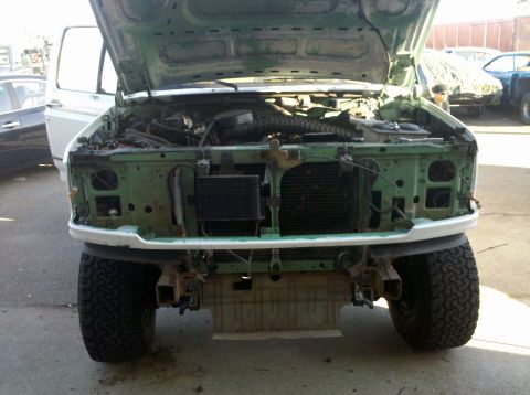 1995 Ford Bronco - The front end of a green Ford truck is shown with its hood up and bumper removed, revealing the engine compartment.