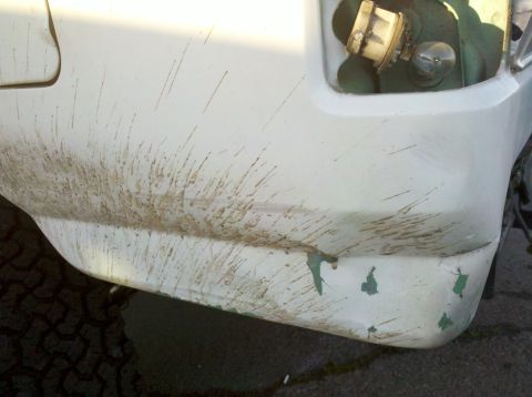 1995 Ford Bronco - The rear corner of a vehicle is covered in mud splatters, revealing green paint underneath chipped white paint.