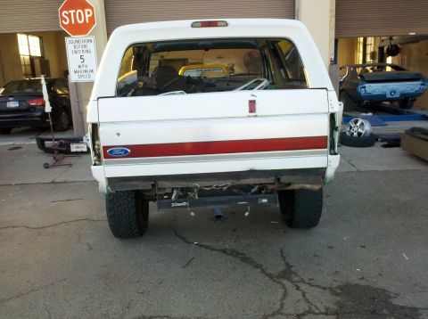 1995 Ford Bronco - Rear view of a white Ford Bronco with a red stripe, missing its tailgate and bumper.