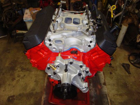 1989 Ford Bronco - A rebuilt V8 engine sits on a red tray, showing its red block, silver intake, and black valve covers.