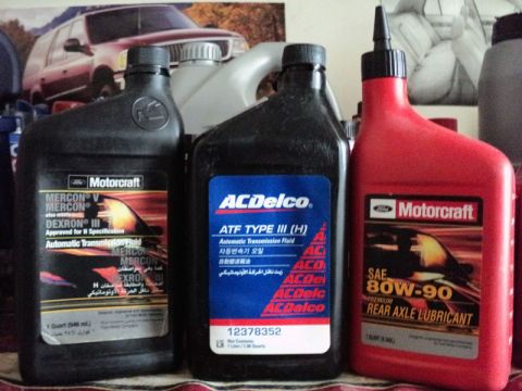1999 Mercury Grand Marquis - A collection of automotive fluids, including transmission fluid and rear axle lubricant, are displayed on a shelf.