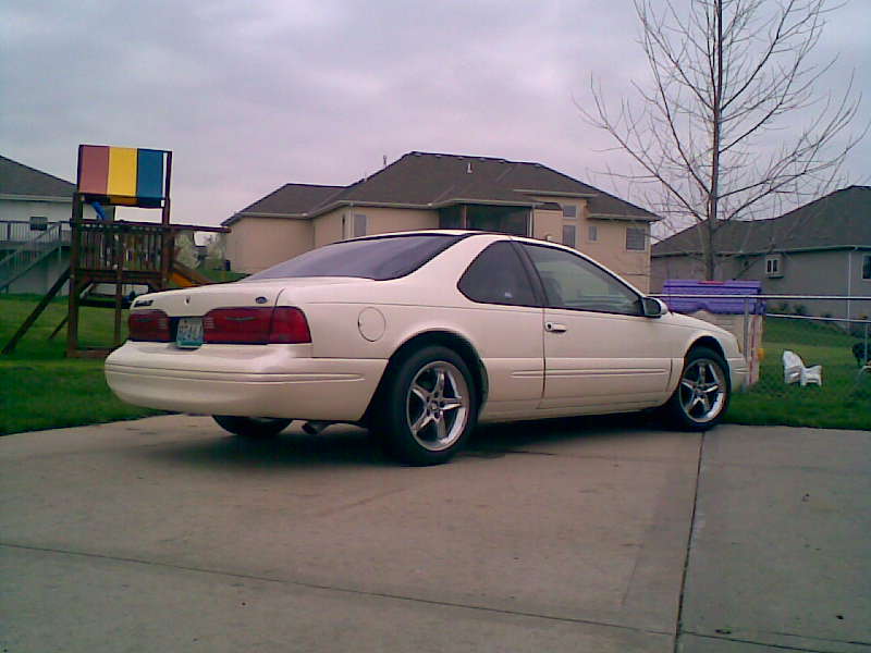 White coupe parked in a suburban driveway. Rear quarter view