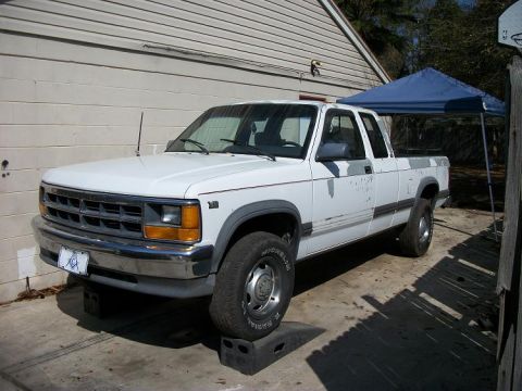 1994 Ford Explorer - A white pickup truck with a dual cab is parked on ramps in front of a building.