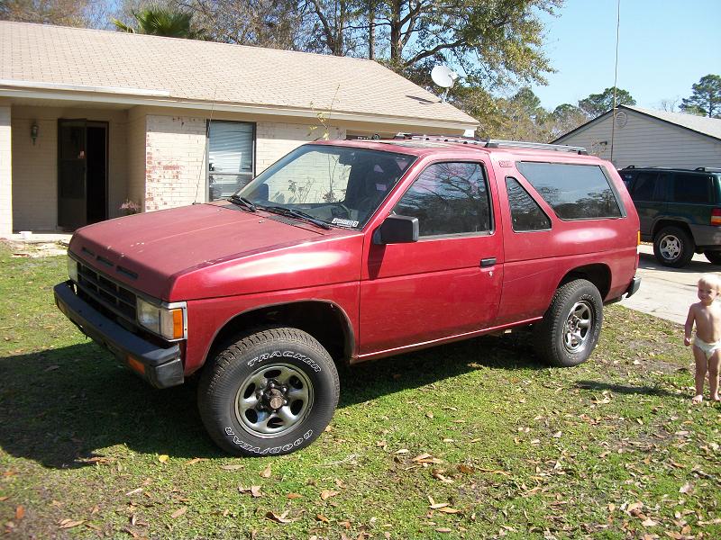 Faded red two-door Nissan Pathfinder SUV parked on grass, 3/4 front view