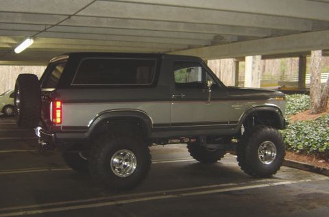 1986 Ford Bronco - This lifted Ford Bronco is parked in a covered lot, showing its side profile and off-road tires.