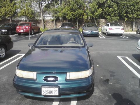 1993 Ford Taurus - A green sedan is parked in a lot with other vehicles around it.