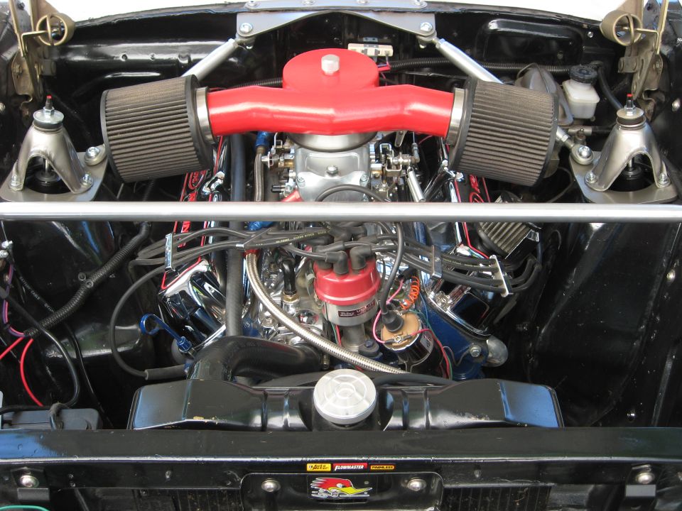 Engine bay of a 1965 Ford Ranchero with a V8 engine, red intake, dual air filters, and chrome accents