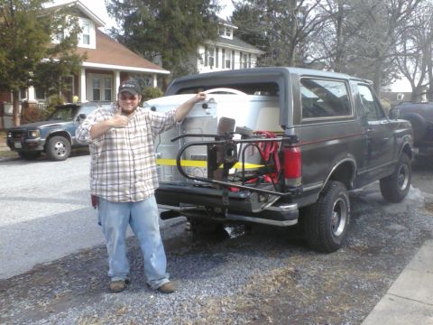1988 Ford Bronco - Man stands with a 1988 Ford Bronco loaded with cargo, another vehicle visible in the background.