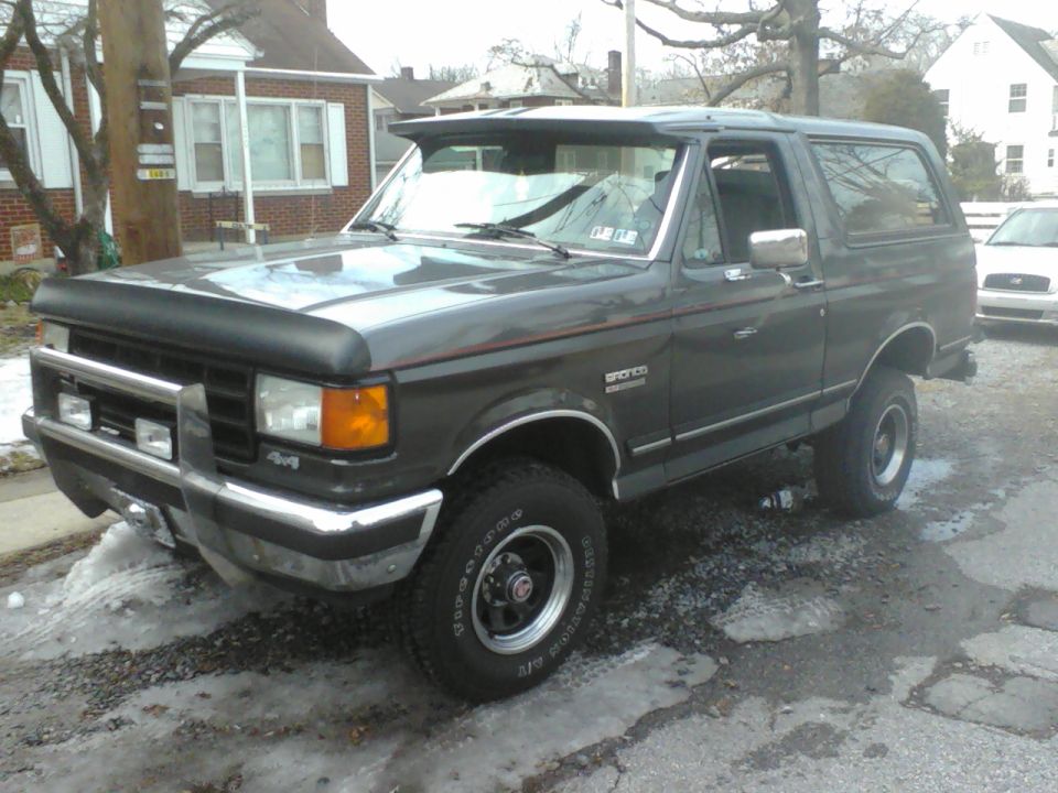 Dark gray Ford Bronco with a bug deflector and chrome bumper. It has 4x4 badging on the front fender