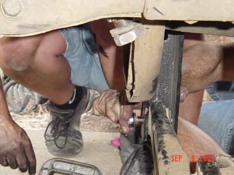1989 Ford Bronco - Two individuals are seen working on the undercarriage of a vehicle, appearing to adjust suspension components.