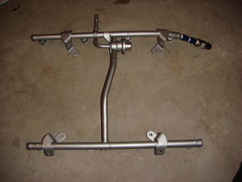 Fuel rail assembly with injectors attached, resting on a concrete floor