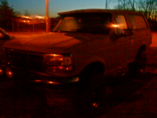 Front 3/4 view of a dark colored Ford Bronco parked outside at dusk