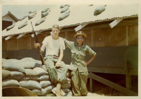 1990 Ford Probe - Two soldiers pose in front of sandbags and a building with a corrugated roof.
