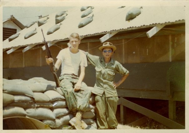 Vintage snapshot of two soldiers posed on sandbags outside a corrugated metal barracks