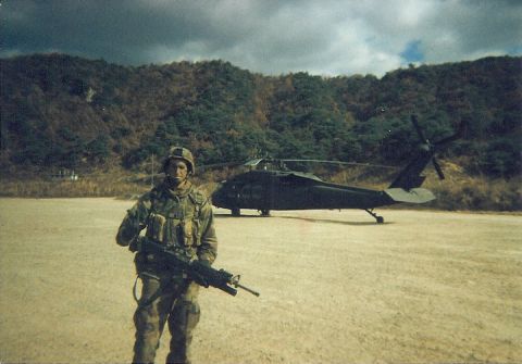 1990 Ford Probe - A soldier stands guard in front of a parked helicopter in a rural, mountainous area.