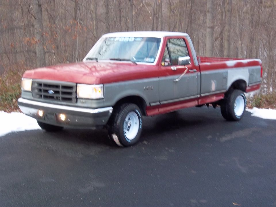 Red and gray two-tone pickup truck parked on asphalt with snow on the ground