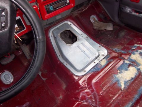 1989 Ford F-150 - The interior floor of a vehicle shows exposed metal and red paint, with the transmission tunnel area open.