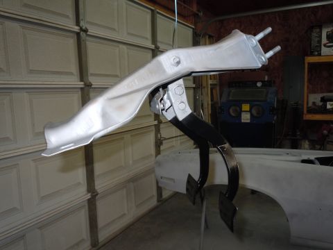 1972 Chevrolet Camaro - A silver pedal assembly hangs in a workshop, with a car body undergoing preparation in the background.