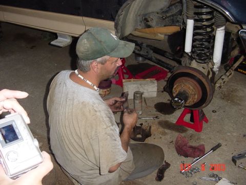 1989 Ford Bronco - A man works on the suspension of a vehicle, with the brake rotor and hub assembly visible.