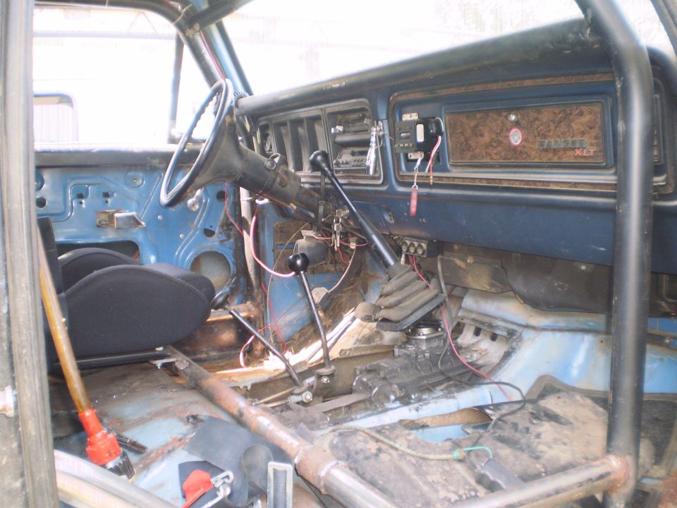 Gutted blue Ford truck interior with roll cage, exposed wiring, and Ranger XLT woodgrain dash.