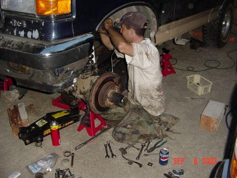 1989 Ford Bronco - A mechanic works on the front suspension of a 1989 Ford Bronco, with tools and parts scattered around.