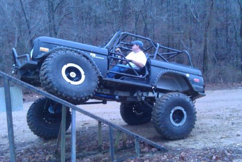 1967 Ford Mustang - A modified black Ford Bronco with oversized tires and a roll cage navigates an incline.