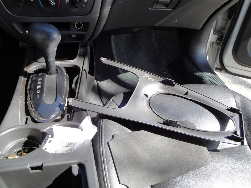 Car interior with gear shift, cup holders, and a removed dashboard trim piece