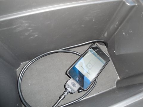 2003 Ford Taurus - An iPhone is plugged into a car accessory within a dark storage compartment.