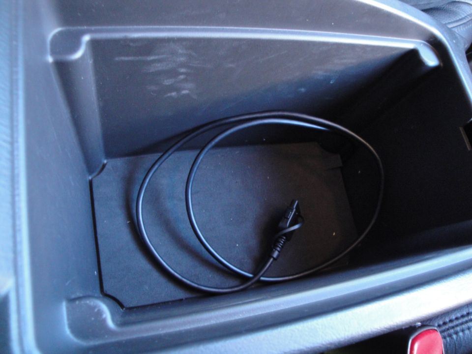 Aux audio cable coiled inside a felt-lined center console storage bin