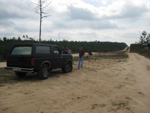 1994 Ford Bronco - A group of people stand near a black Ford Bronco on a sandy dirt road in a wooded area.