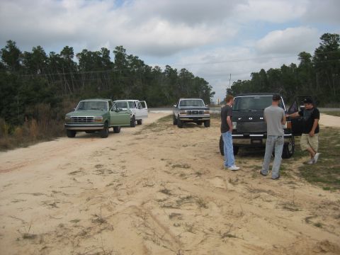 1994 Ford Bronco - Several trucks are parked on a dirt road in a wooded area, with people gathered around one of the vehicles.