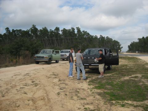1994 Ford Bronco - Three Ford Broncos are parked on a dirt road in a wooded area, with several people gathered around one of the vehicles.