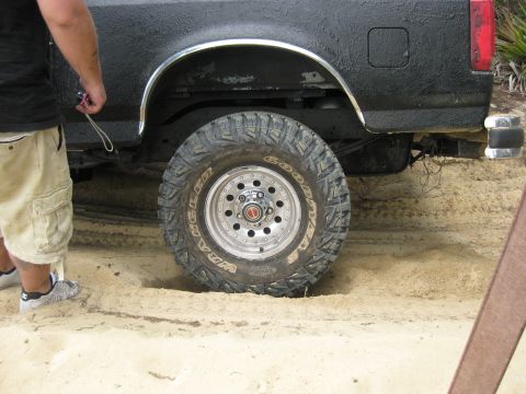 1994 Ford Bronco - A black Ford Bronco is stuck in the sand, showing its rear tire and fender.