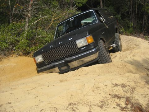 1994 Ford Bronco - Black Ford Bronco navigating a sandy incline, showing off its off-road capabilities.