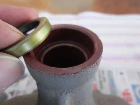 1979 Ford Bronco - A hand holds a metal seal over a dark red housing, preparing for installation.