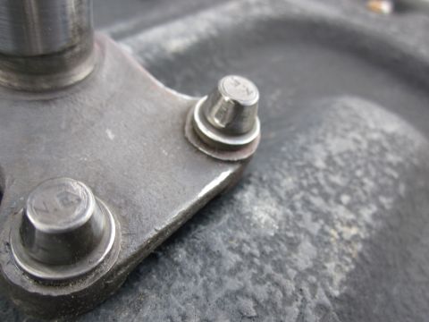 1979 Ford Bronco - Close-up of a metal bracket with two bolts, each bearing the marking 'NE'.
