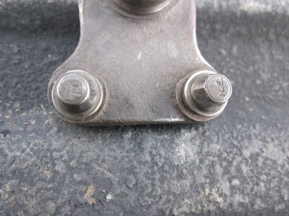 Close-up of a metal bracket with two bolts, one bolt head has faint markings