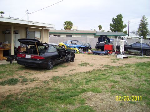 1995 Ford Probe - Several vehicles are in various states of disassembly in a residential yard.