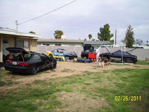 1995 Ford Probe - Multiple vehicles, including a black 1995 Ford Probe, are in various states of disassembly in a residential yard.