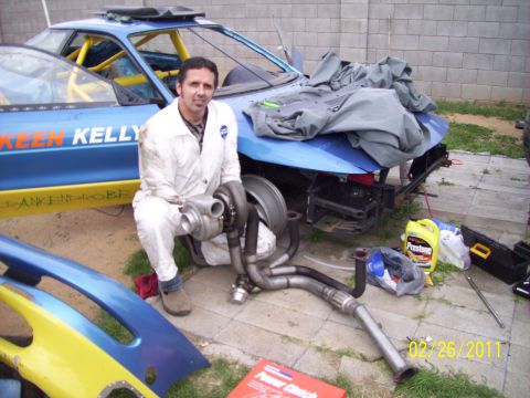 1995 Ford Probe - A man kneels with a turbocharger in front of a heavily modified blue car, which has custom text on its side.